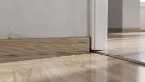 Sopralluogo ravvicinato su battiscopa in legno e bordo parquet con dettagli tecnici lungo il perimetro di una stanza